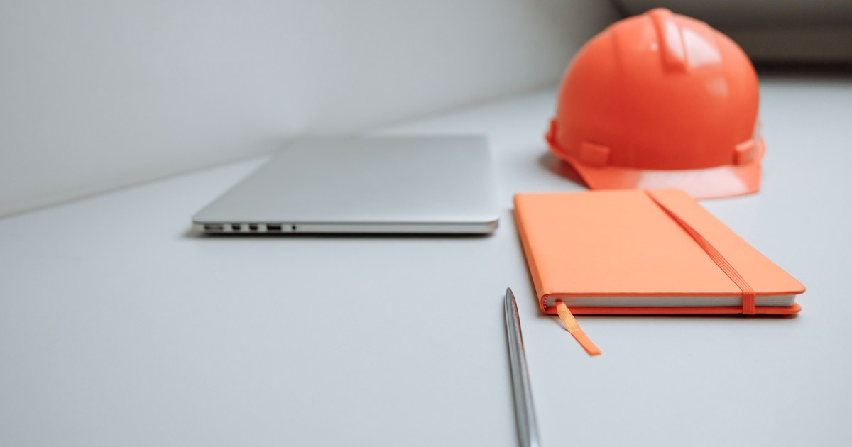 Laptop, notebook, and construction hard hat on an office desk